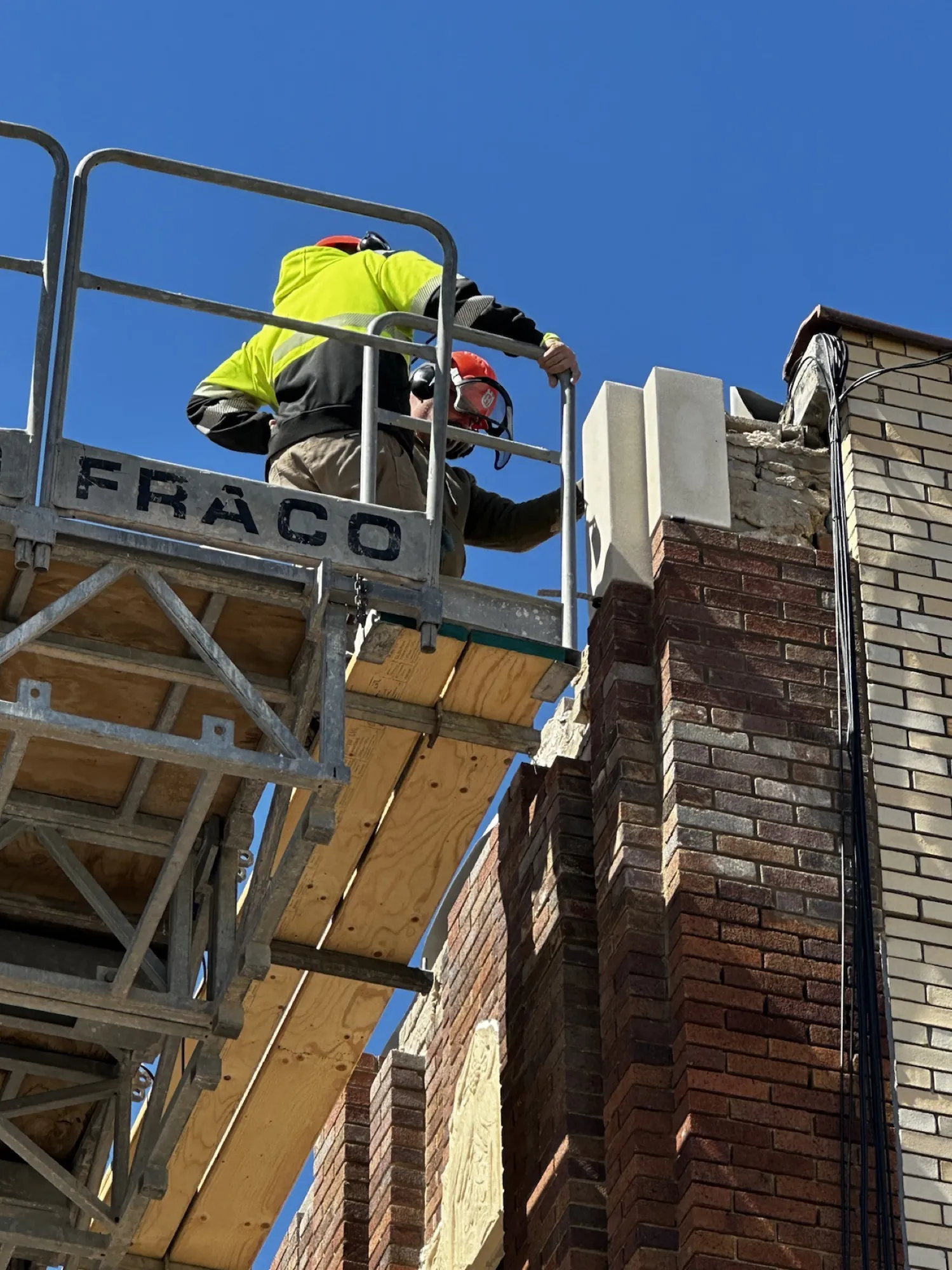 Setting new cast stone at the parapet, three stories above a working downtown street.